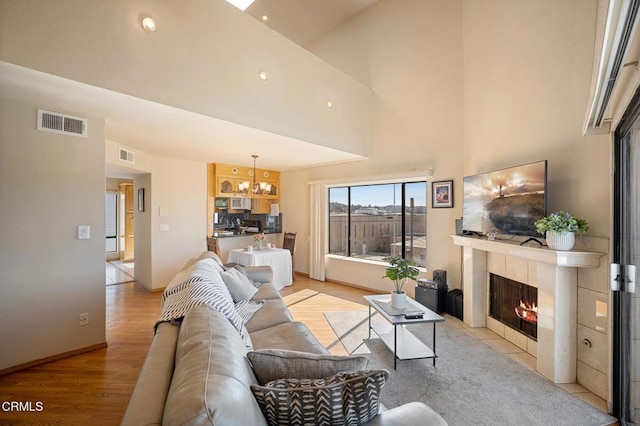 living room featuring a tiled fireplace, a high ceiling, a chandelier, and light wood-type flooring