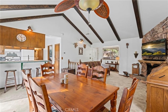 dining space with ceiling fan, high vaulted ceiling, light carpet, a stone fireplace, and beamed ceiling