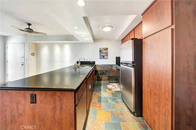 kitchen featuring stainless steel refrigerator, sink, oven, ceiling fan, and a raised ceiling