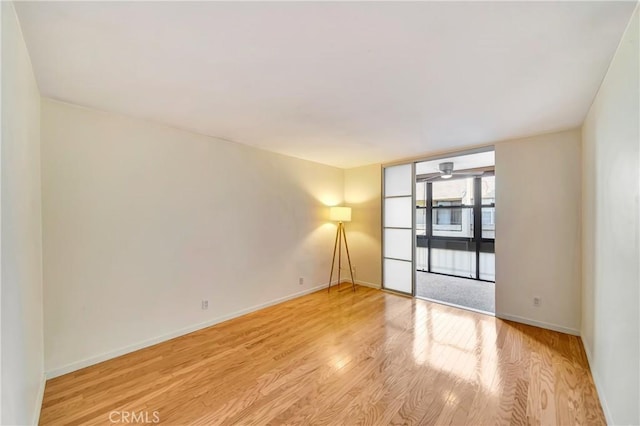 unfurnished room featuring ceiling fan, a wall of windows, and light wood-type flooring