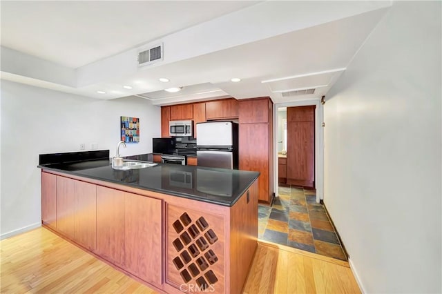 kitchen with light hardwood / wood-style floors, appliances with stainless steel finishes, kitchen peninsula, and sink