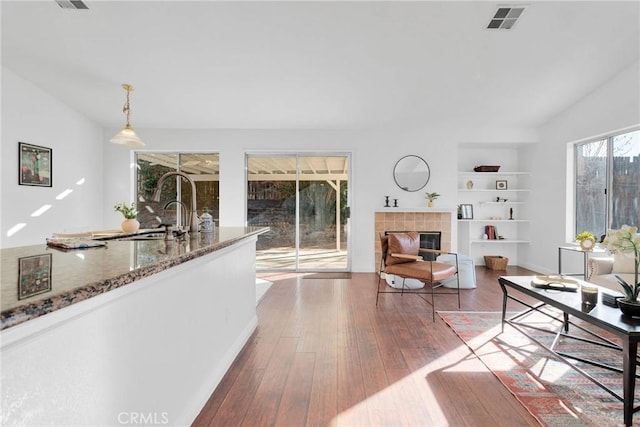 living room featuring a tile fireplace, vaulted ceiling, hardwood / wood-style floors, built in features, and sink