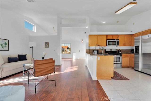 kitchen with sink, high vaulted ceiling, dark stone counters, and appliances with stainless steel finishes