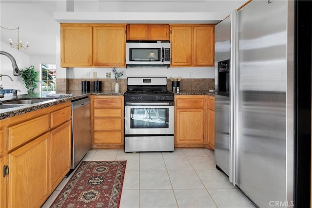 kitchen with stainless steel appliances, sink, dark stone counters, and light tile patterned floors