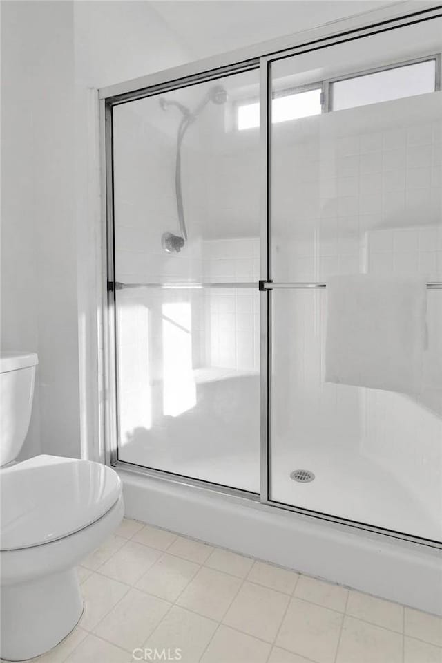 bathroom with a shower with shower door, tile patterned floors, and toilet