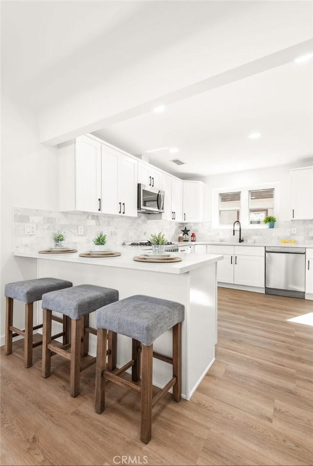 kitchen with appliances with stainless steel finishes, a breakfast bar, white cabinets, and kitchen peninsula