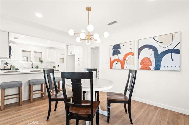 dining room with sink, a chandelier, and light wood-type flooring