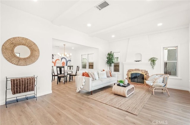 living room with a notable chandelier, beam ceiling, light hardwood / wood-style floors, and a large fireplace