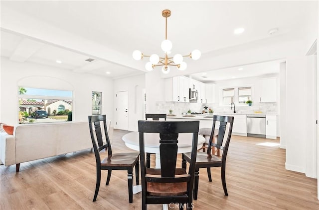 dining room with beamed ceiling, a chandelier, sink, and light hardwood / wood-style flooring