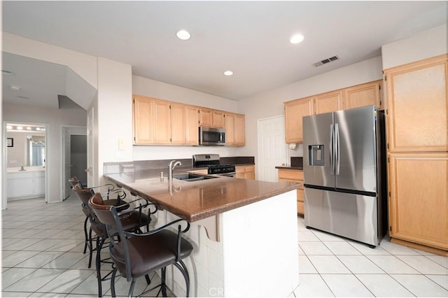 kitchen with appliances with stainless steel finishes, kitchen peninsula, sink, and light brown cabinets