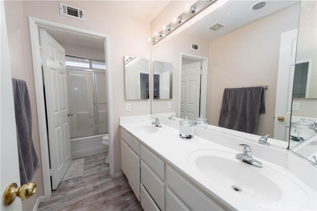 full bathroom with hardwood / wood-style flooring, vanity, shower / bath combination with glass door, and toilet