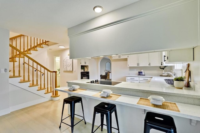 kitchen with a breakfast bar area, light stone counters, black appliances, white cabinets, and kitchen peninsula