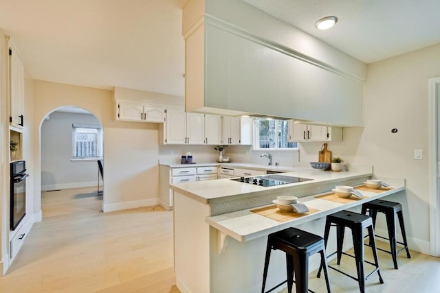 kitchen with a kitchen bar, kitchen peninsula, white cabinets, a healthy amount of sunlight, and black appliances