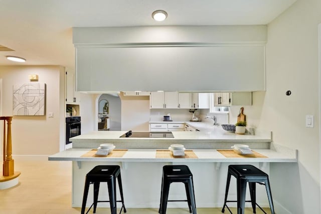 kitchen with black appliances, kitchen peninsula, white cabinets, and a breakfast bar