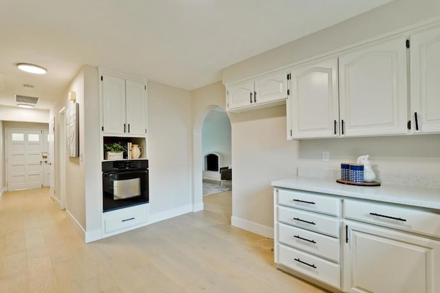 kitchen with white cabinetry, black oven, and light hardwood / wood-style floors