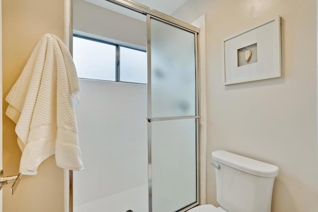 bathroom featuring a shower with shower door and toilet