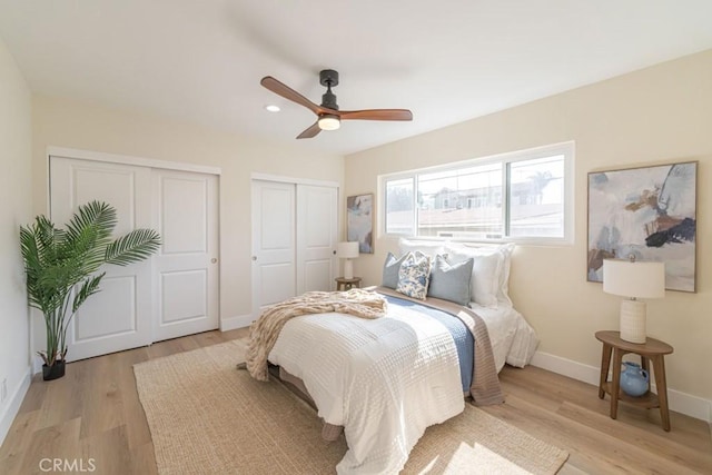 bedroom featuring ceiling fan, light hardwood / wood-style floors, and multiple closets