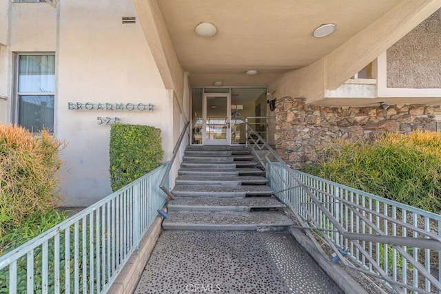 entrance to property with stone siding, visible vents, and stucco siding