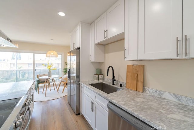 kitchen featuring stainless steel appliances, a sink, white cabinetry, light wood-type flooring, and light stone countertops