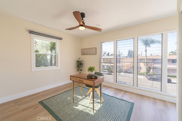 office featuring baseboards, light wood-type flooring, a ceiling fan, and a healthy amount of sunlight