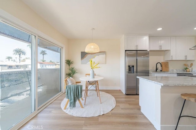 kitchen featuring pendant lighting, stainless steel fridge, light hardwood / wood-style flooring, light stone counters, and white cabinets