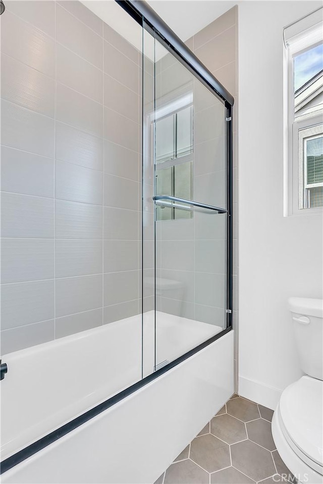 bathroom with tile patterned floors, shower / bath combination with glass door, and toilet