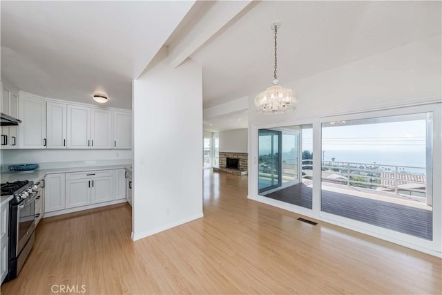 kitchen with pendant lighting, stainless steel range with gas stovetop, light hardwood / wood-style floors, and white cabinets