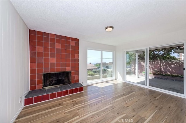 unfurnished living room with a tiled fireplace, hardwood / wood-style floors, and a textured ceiling