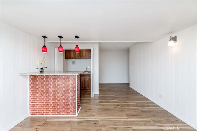 bar featuring hardwood / wood-style flooring, light stone countertops, sink, and pendant lighting