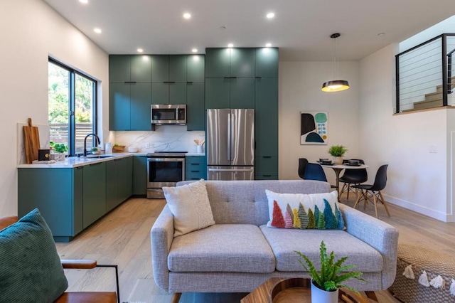 kitchen with appliances with stainless steel finishes, decorative light fixtures, sink, backsplash, and light hardwood / wood-style flooring