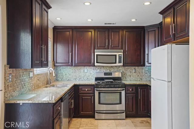 kitchen featuring sink, light tile patterned floors, appliances with stainless steel finishes, light stone countertops, and backsplash