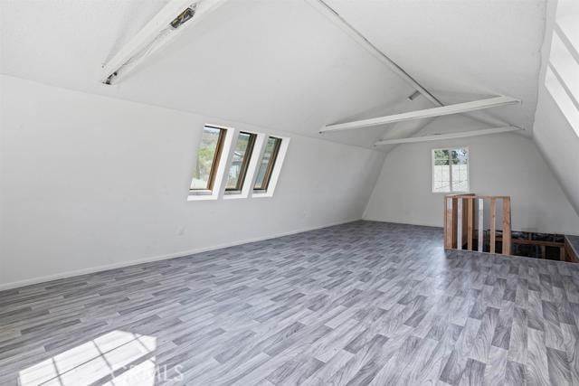 bonus room with lofted ceiling with beams and light wood-type flooring