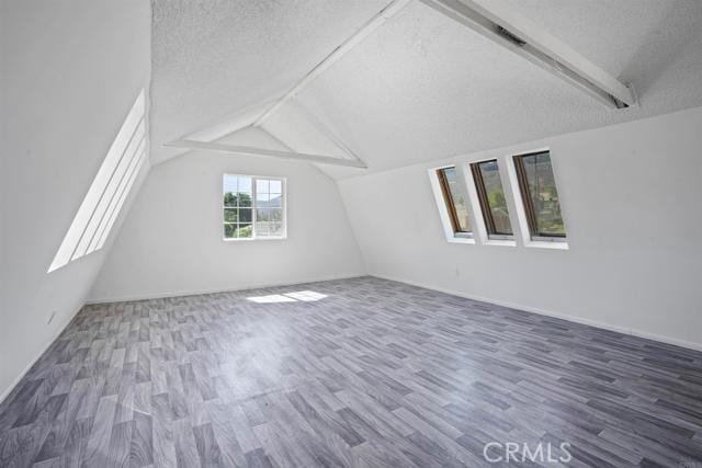 additional living space featuring dark wood-type flooring, lofted ceiling with beams, and a textured ceiling