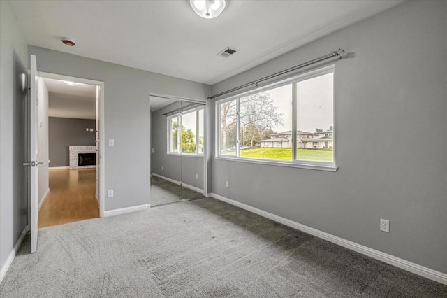 unfurnished bedroom featuring a brick fireplace, carpet floors, and a closet