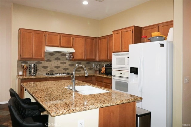 kitchen featuring sink, tasteful backsplash, a kitchen breakfast bar, white appliances, and light stone countertops