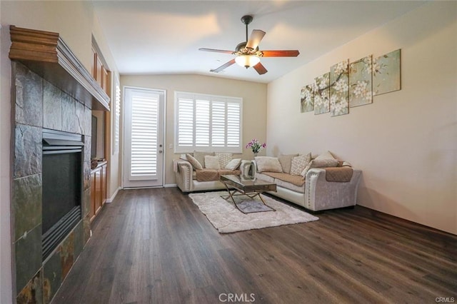 living room featuring a tiled fireplace, lofted ceiling, dark wood-type flooring, and ceiling fan