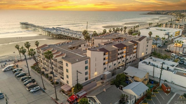 aerial view at dusk with a water view and a beach view