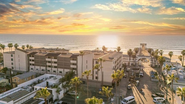 aerial view at dusk featuring a water view and a view of the beach