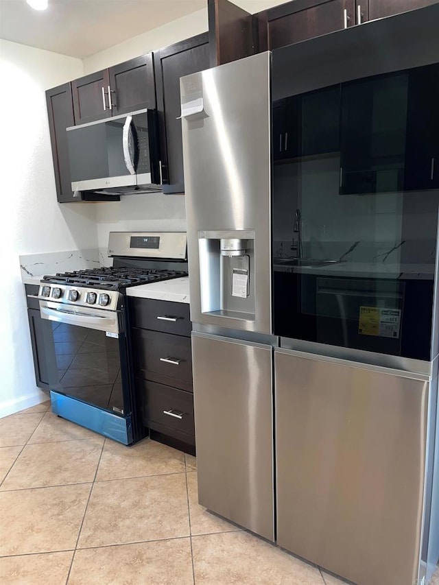 kitchen featuring light tile patterned floors, appliances with stainless steel finishes, dark brown cabinetry, and light stone countertops