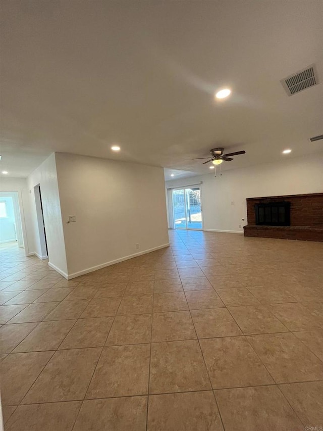 empty room with a brick fireplace, visible vents, ceiling fan, and light tile patterned flooring