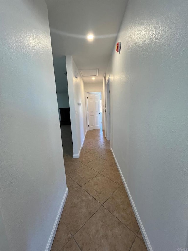 hall featuring attic access, baseboards, and tile patterned floors