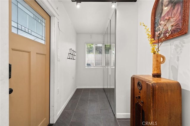 hallway featuring baseboards and dark tile patterned flooring