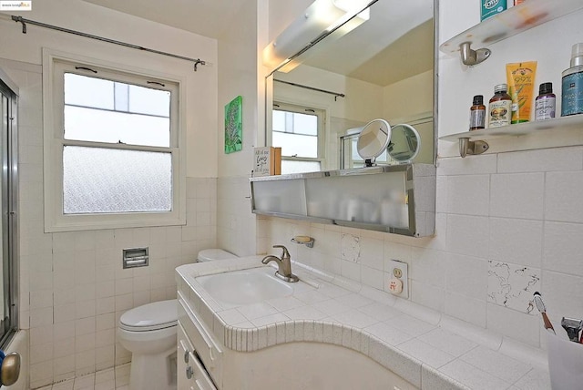 full bathroom featuring vanity, combined bath / shower with glass door, tile walls, and toilet