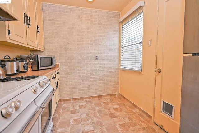 kitchen with brick wall, a healthy amount of sunlight, and white range with gas stovetop