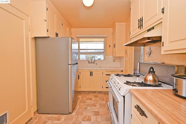 kitchen featuring sink, stainless steel refrigerator, white range with gas cooktop, white cabinets, and backsplash