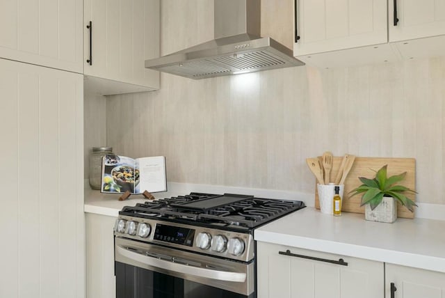 kitchen with wall chimney range hood, stainless steel gas range oven, and white cabinets