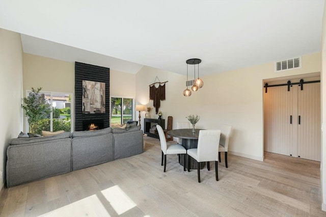 dining room featuring a large fireplace, light hardwood / wood-style flooring, and a barn door