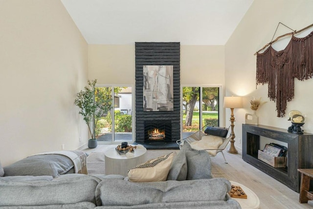 living room featuring high vaulted ceiling, a healthy amount of sunlight, a fireplace, and light hardwood / wood-style floors