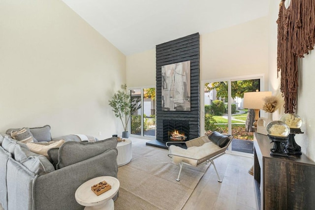 living room featuring a healthy amount of sunlight, a fireplace, high vaulted ceiling, and light hardwood / wood-style flooring