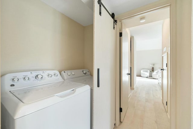 clothes washing area with a barn door, washer and dryer, and light hardwood / wood-style floors